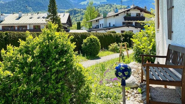 A garden with a bench, a globe decoration, and a mountain view.