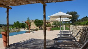 A patio area with lounge chairs and umbrellas, a pool, and a stone wall. - Sauvignon (Robion)
