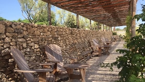 A covered outdoor seating area with wooden chairs and tables, a stone wall, and a gravel path. - Sauvignon (Robion)