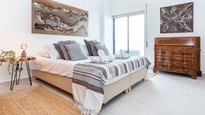 Ein modernes Schlafzimmer mit einem Bett, einer Holzkommode und zwei abstrakten Bildern.
