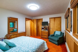 Quarto com cama, cômoda, suporte para TV e uma cadeira.