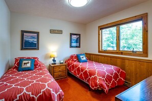 A room with two beds, a nightstand, a lamp, and a window with a view of trees.