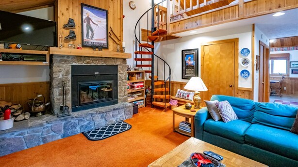 A cozy living room with a stone fireplace, a blue sofa, a wooden staircase, and a television on the wall. - 2 bedroom accommodation in Davis (Davis)