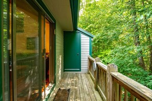 A wooden deck with a green door and a window overlooking a forested area.
