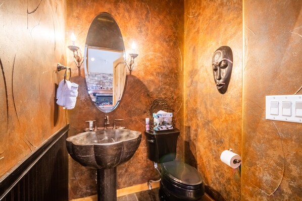 A bathroom with a marble sink, a toilet, a mirror, and a wall-mounted light fixture.