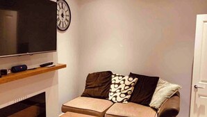 A living room with a sofa, a coffee table, a flat-screen TV, and a clock on the wall. - Breeze on Southend in Essex (Southend-on-Sea)