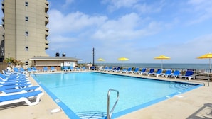 Ein Swimmingpool mit blauen Liegestühlen und gelben Sonnenschirmen, ein Gebäude mit flachem Dach und ein klarer Himmel.