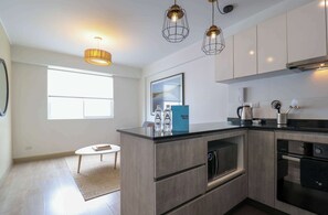 Une cuisine moderne dotée d’un îlot central, d’un four encastré et de luminaires suspendus.
