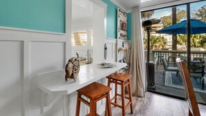 Une cuisine dotée d’un plan de travail blanc, de tabourets en bois et offrant une vue sur le patio extérieur avec ses parasols.