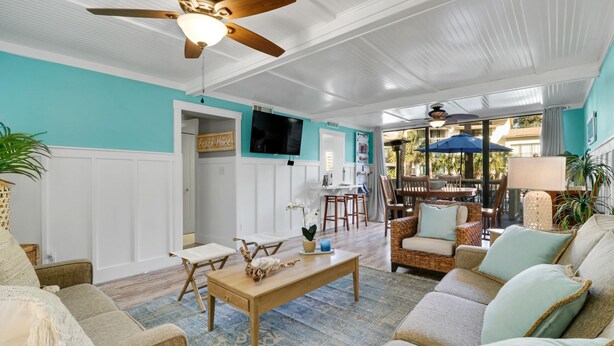 Un vaste salon doté d’un ventilateur de plafond, un coin repas avec une table et des chaises, et une vue sur la terrasse extérieure.