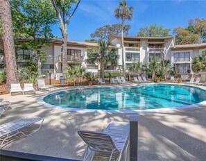 A pool area with lounge chairs and palm trees. - Charming Beach Townhome! Short walk to the Beach and Coligny Plaza. (Hilton Head Island)