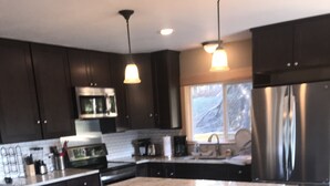 A modern kitchen with dark cabinetry, a large island with stools, stainless steel appliances, and pendant lighting. - Great for Families & Groups! (Windham,)