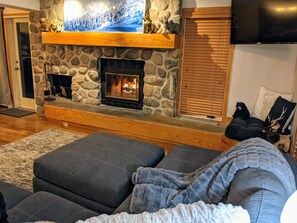 Ein gemütliches Wohnzimmer mit Kamin aus Stein, einem Flachbildfernseher und einer bequemen Sitzecke.