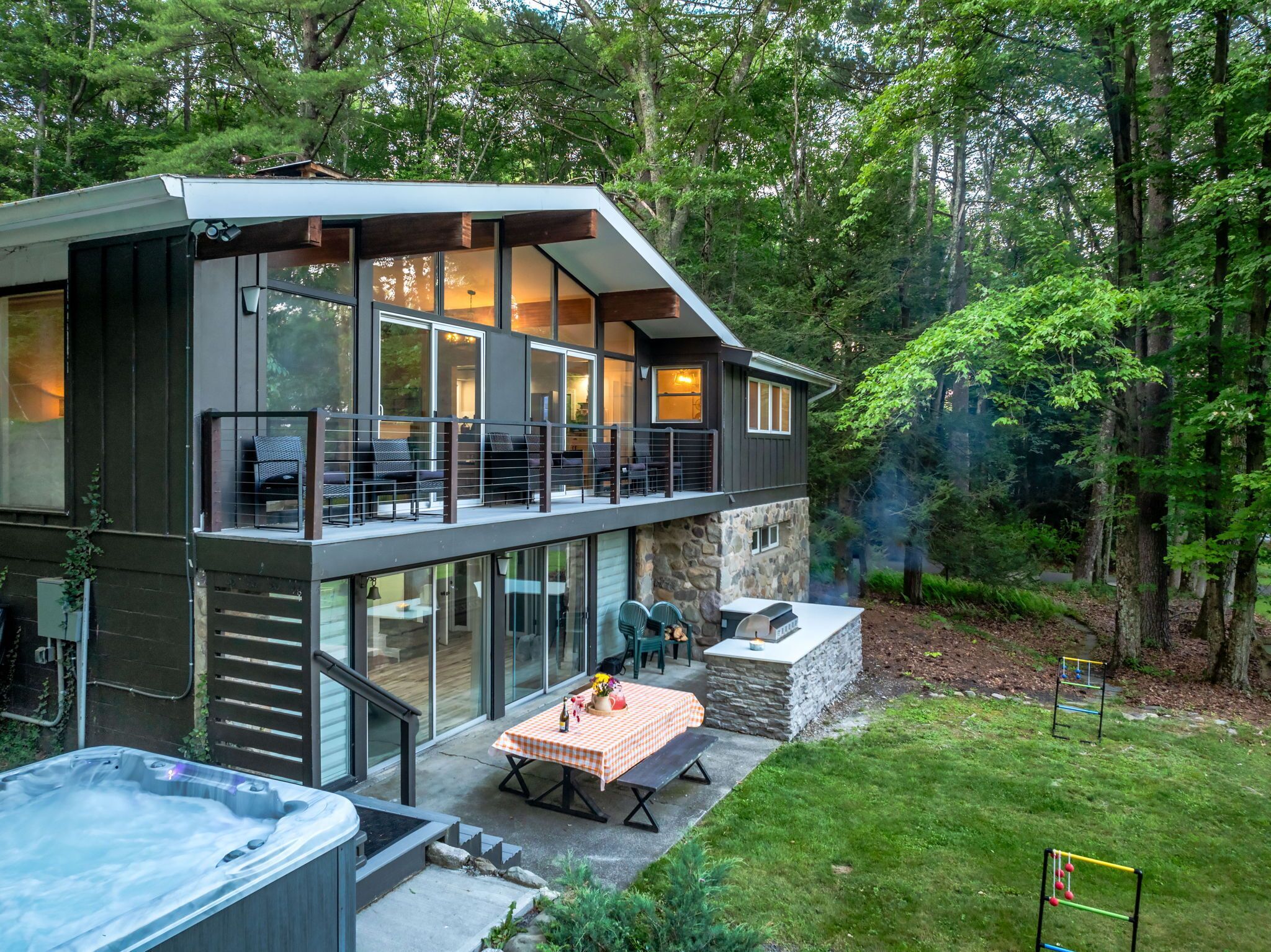 A modern two-story house with a balcony, a hot tub, and a patio with a table and chairs.