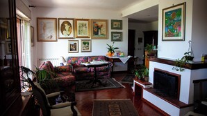 A living room with a sofa, armchairs, a fireplace, and various framed artworks on the walls.