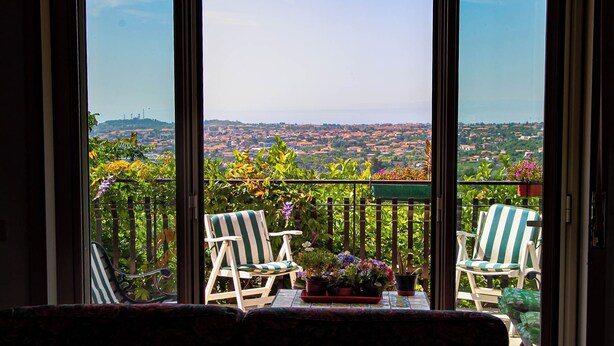 A balcony with two striped chairs, a small table with potted plants, and a view of a cityscape.