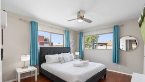 Une chambre à coucher bien aménagée, avec un grand lit, un ventilateur de plafond et une vue sur l’extérieur par une fenêtre.