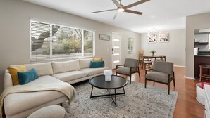 Un salon comprenant un canapé, une table basse et des fauteuils, un ventilateur de plafond, ainsi qu’un coin repas avec une table et des chaises.