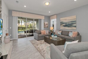 Relax in this stylish living room with a sofa, abstract art, and a glass door leading to a patio with outdoor furniture.