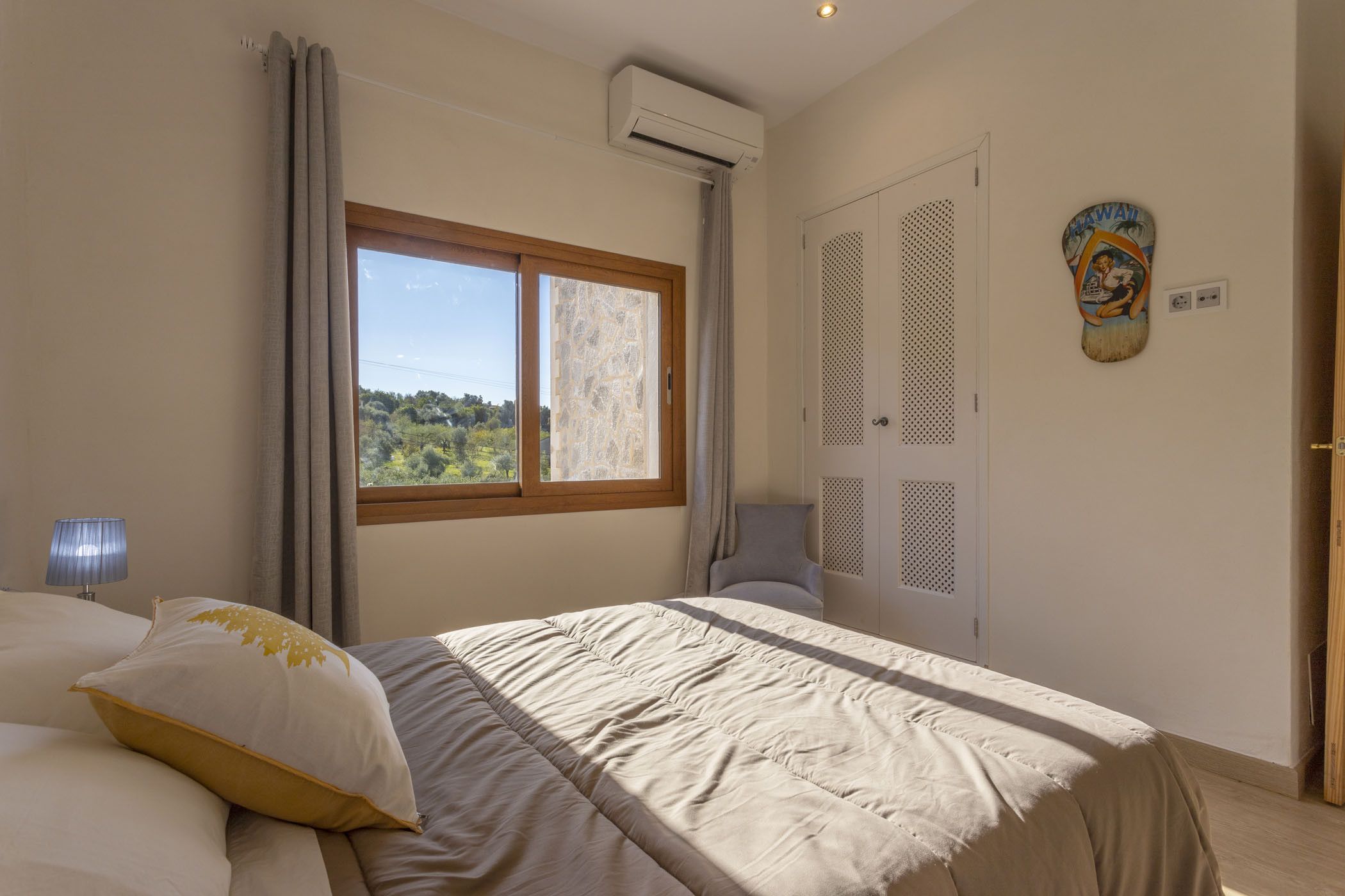 A bedroom with a bed, a window, an air conditioning unit, a door, and a wall decoration.