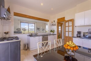 A modern kitchen with white cabinets, a central island, and a dining area with a glass table. - Modern villa with 3 bedrooms, 2 bathrooms, wifi, terraces and pool (Inca)