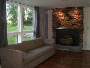 A living room with a stone fireplace, a sofa, and a large window with curtains.