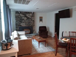A living room with a stone fireplace, a sofa, a recliner, a dining table with chairs, and a kitchen area with a stove.