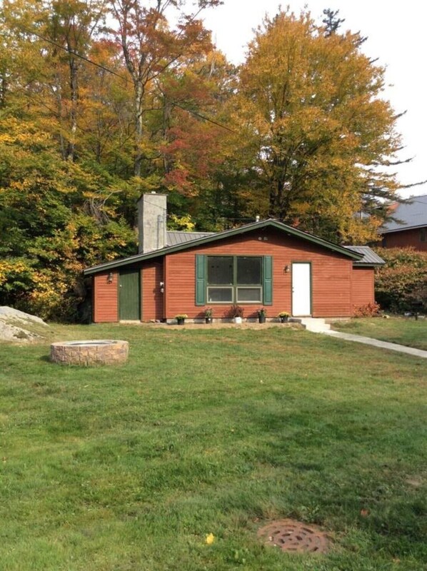 A small, single-story wooden cabin with a chimney, a front door, and a window.