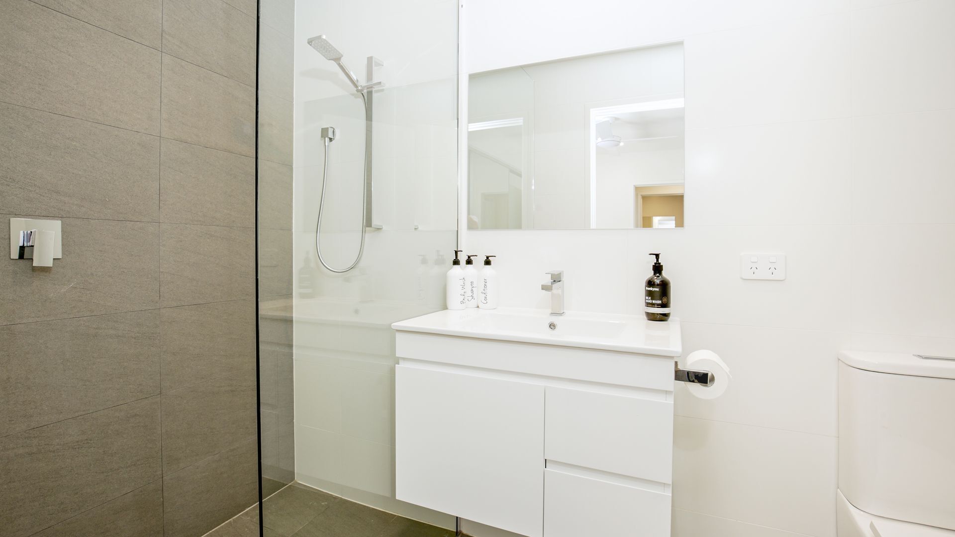 Un baño moderno con cabina de ducha de vidrio, tocador blanco con espejo y un inodoro.