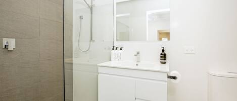 Un baño moderno con cabina de ducha de vidrio, tocador blanco con espejo y un inodoro.