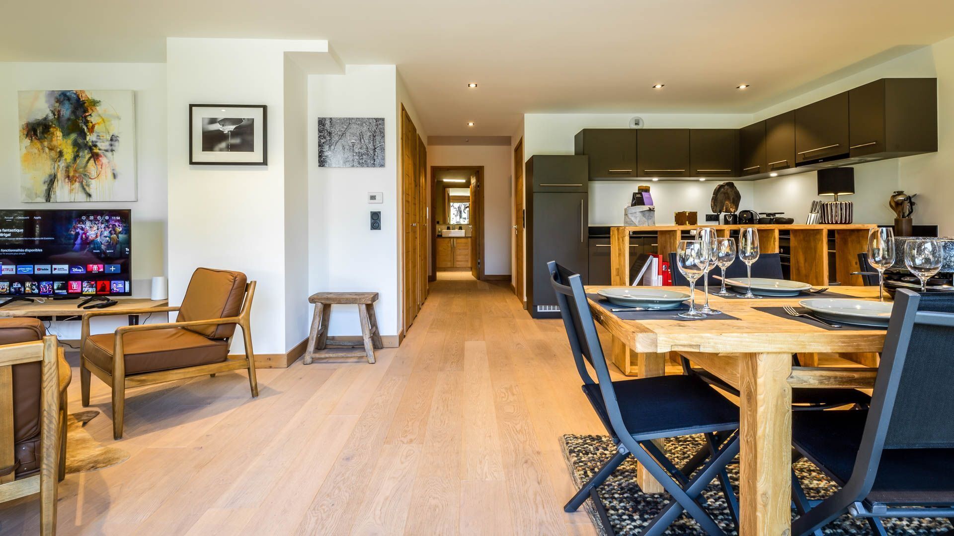 Una cocina moderna con armarios oscuros, una mesa de madera para cuatro personas y un televisor que muestra una película.