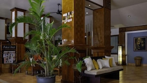 A lobby with a reception desk, a large potted plant, a sofa with cushions, and a wooden column. - Pakse Hotel (Pakse)