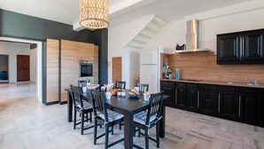 Una cocina moderna con comedor, que presenta un gran mesa de madera, sillas negras y una lámpara colgante.