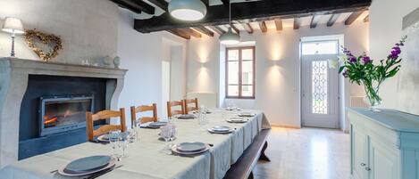 A dining area with a long table set for a meal, a fireplace, and a view through a window.