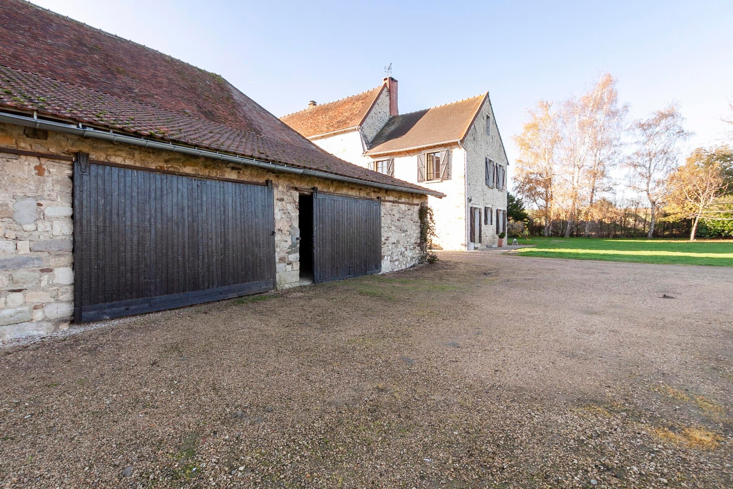 A stone building with two large garage doors, a gravel driveway, and a grassy area with trees.