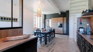 Una cocina moderna con armarios de madera, una zona de comedor con sillas y una lámpara colgante.