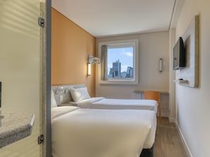 Een hotelkamer met twee bedden, uitzicht op de stad, een televisie en een klein tafeltje.