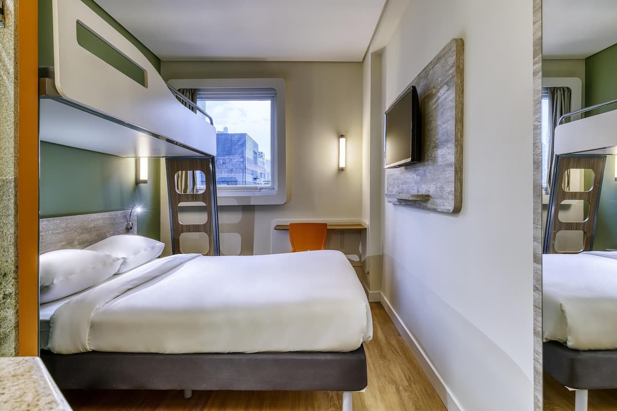 Habitación de hotel pequeña con literas, un escritorio, televisión y ventana con vistas a la ciudad.