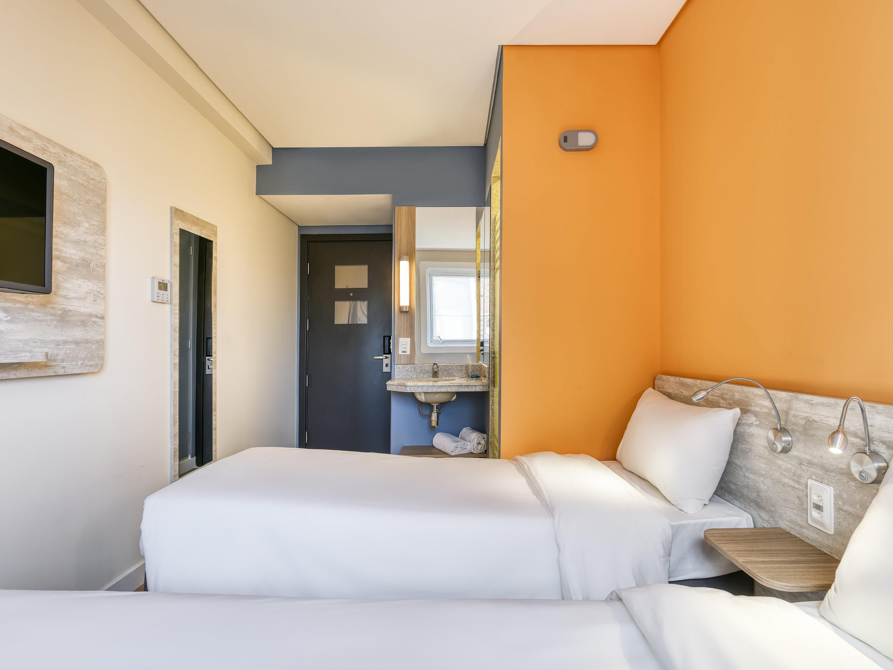 A hotel room with two beds, a bathroom with a sink, and a mirror.
