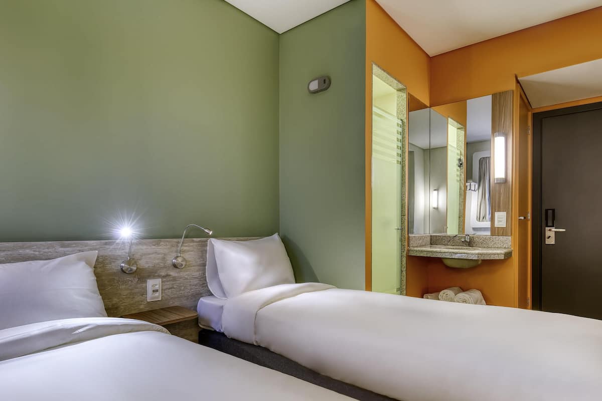 Una habitación de hotel con dos camas, una mesita de noche, una lámpara, un espejo y una puerta.