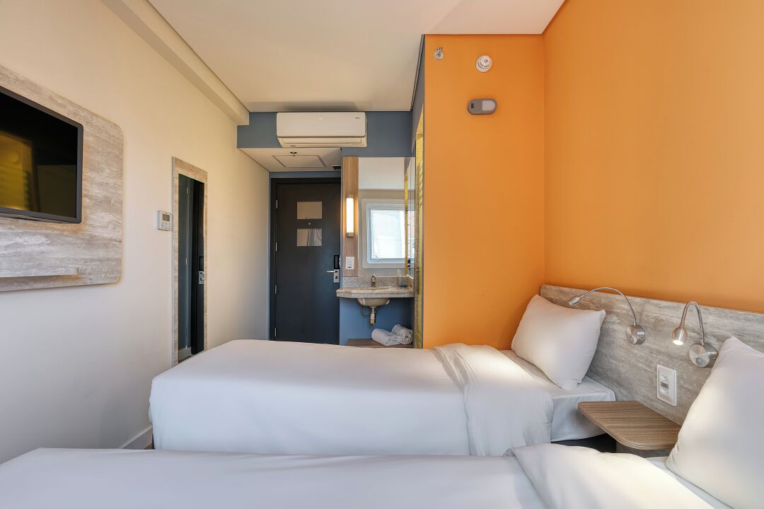 Quarto de hotel com duas camas, banheiro com pia e ar condicionado.