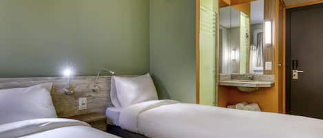 A hotel room with two beds, a nightstand, a lamp, a mirror, and a door.