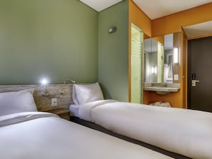 Ein Hotelzimmer mit zwei Betten, einem Nachttisch, einer Lampe, einem Spiegel und einer Tür.