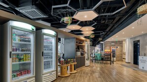 Un intérieur moderne avec des luminaires hexagonaux au plafond, des distributeurs de boissons réfrigérés, des tables en bois et un espace salon.