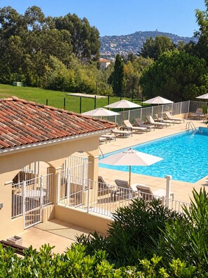 A swimming pool with lounge chairs and umbrellas, surrounded by a fence and greenery.
