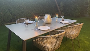 Ein Essbereich im Freien mit einem Tisch für zwei Personen, umgeben von Korbstühlen, mit Kerze und Gläsern auf dem Tisch.