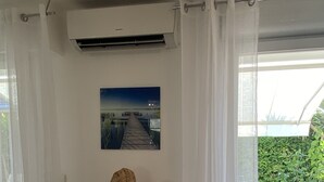 Ein Zimmer mit einer großen Kaktusskulptur, einem Bild an der Wand und Blick auf einen Garten durch transparente Vorhänge.