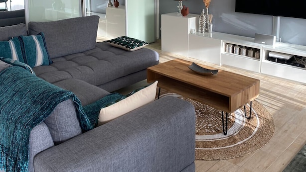 Ein modernes Wohnzimmer mit einem grauen Sofa, einem Holztisch und einem an der Wand befestigten Flachbildfernseher.