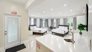Moderni hotellihuone, jossa on kaksi sänkyä, pesuallas, pieni pöytä ja näkymä vihreälle alueelle.