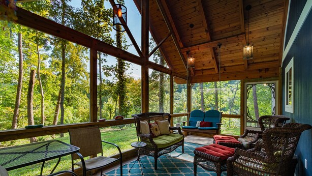 A covered outdoor seating area with wicker furniture, a table, and a view of the surrounding forest. - Southern Charm in Smoky Mountain Seclusion (Bryson City)